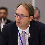 Middle aged man, in blue suite with blond hair and wearing glasses.